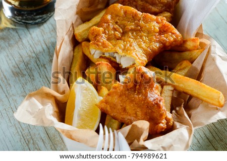 Fish and chips in a paper wrapper. Ruddy crust of batter, lemon slice for squeezing juice. Yummy takeaway food. Royalty-Free Stock Photo #794989621