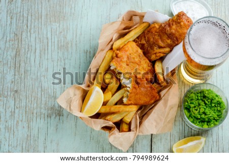 Deep fried fish and chips in combination with lemon slices, green peas and beer on a rustic table. Feed your tummy with yummy food. Royalty-Free Stock Photo #794989624