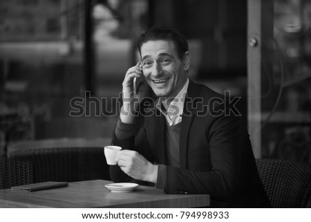 Portrait of happy male speaking by phone while sitting at table in cafe. Black and white photo. Relax and communication concept