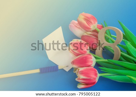 International Women's Day concept. Tulips and wooden eight figure, greeting card with a pencil on the blue background. 