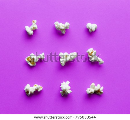 White popcorn in different shapes and forms on trendy purple background, top view. Many corn elements for graphic design.