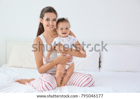 Mother and cute baby after bathing sitting on bed at home