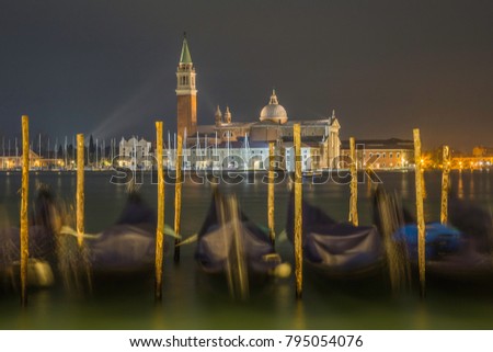 Swinging tied gondolas at night in the port of the Grand Canal in the background lit monastery of San Giorgio Maggiore, Venice, Italy. Silky light.