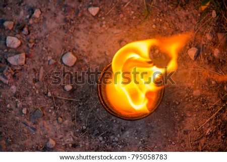 Macro shot of lit candle burning with soft glowing flame and smoke on gravel background. Candle path at the park close to the seaside during the Night of ancient lights