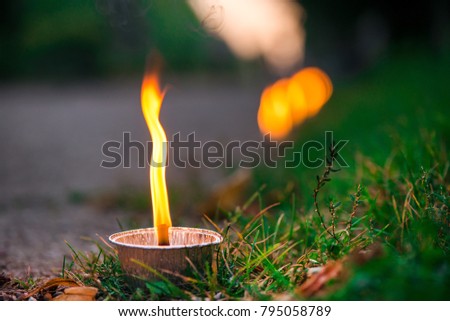 Macro shot of lit candle burning with soft glowing flame and smoke on evening background. Candle path at the park close to the seaside during the Night of ancient lights