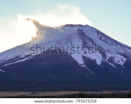 Mount Fuji - A perfect shaped mountain, and iconic symbol of Japan. Telephoto view of the snow cap, detailed enough to see climbing paths. Sudden snow drift spike lit up by the sun setting behind it.