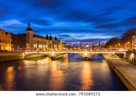 Paris city center by night with embankments of river Seine and illuminated street and historical Parisian building of Conciergerie on City island, blue hour, France.