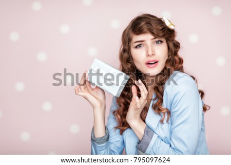beautiful smiling woman in blue jacket holds gift box on pink background. holiday and fun