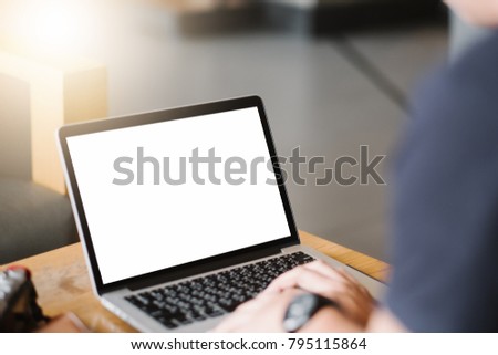 Mockup image of business man using and typing on laptop with blank white screen and coffee cup on glass table in modern loft cafe, Soft focus on vintage wooden table.