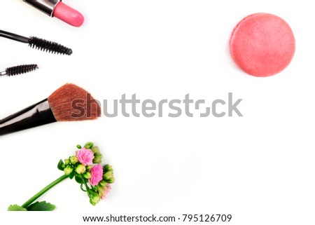 Makeup brush, lipstick, and a mascara applicator, shot from above on a white background with a pink flower, a macaroon, and copy space. A template for a makeup artist's business card or flyer design