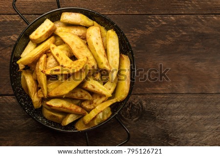 A photo of crunchy potatoes, roasted with salt and garlic, in a skillet, shot from above on a dark wooden background with a place for text