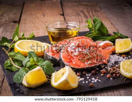 Raw fresh salmon fish before preparing , with olive oil, rosemary, mint, salt, spices,  on old wooden table, vertical