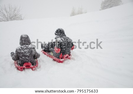 Funny moments in the snow. Two children hurl themselves with their sleds from a snowy slope during a snowfall.