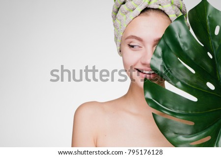 happy young girl with a towel on her head holds a green leaf, thinks about beauty