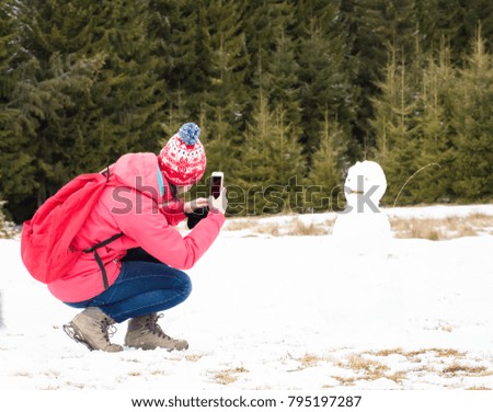 Girl taking a photo of a snowman with a smartphone