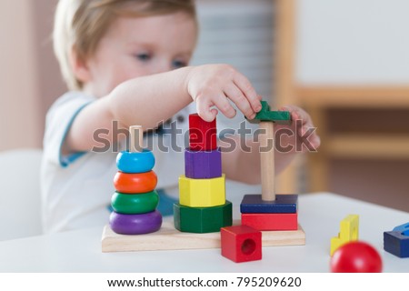 Two years old child boy playing with wooden colorful blocks and sorting shapes at home. educational toys concept. Development of kids fine motor skills, imagination and logical thinking Royalty-Free Stock Photo #795209620