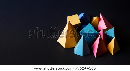 Colorful minimalistic composition abstract geometric solid figures on black textured paper background. Pyramid prism rectangular cube yellow blue pink green colored figures. shallow depth of field,