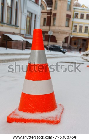Orange and white reflective road cone on the snowy street close up
