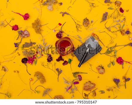 Cup of red tea with book, magnifer and herbs with flowers around on yellow background