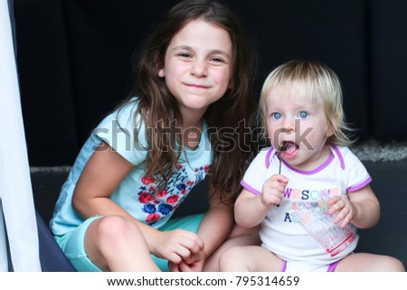 Cute little children 
Dark Hair and Blond Hair are sitting on the Floor Eating Fruits together. Happy girls at home. Funny lovely sisters are having fun in living room. Happy Family Concept 