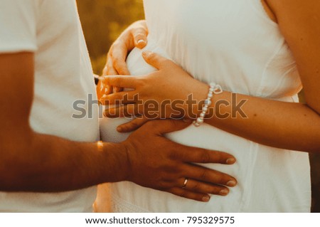 Belly of a pregnant woman. Couple With Pregnant Woman holding hands at sunset standing in a field.  beautiful pregnant woman in wreath relaxing in the summer nature.unrecognizable young pregnant woman