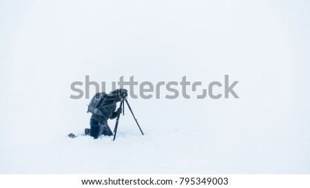 Photographer kneeling in the snow taking photo of winter landscape using a tripod.