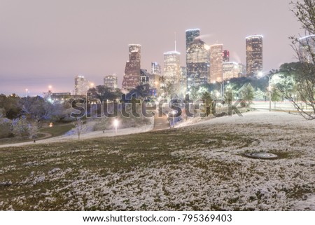 Downtown Houston at  twilight with big and fluffy snowflakes fell on meadow grass at Eleanor Tinsley Park. Park lawn, curved bike pathway, modern skylines in background. Snow is extremely rarely here