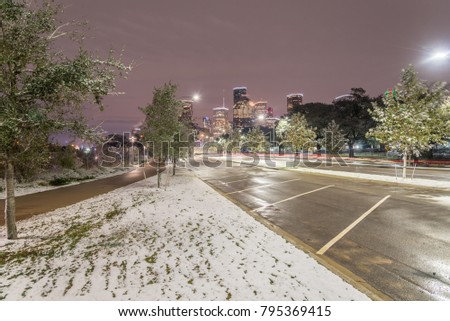 Downtown Houston at  night with big and fluffy snowflakes fell on grass near parking lots at Eleanor Tinsley Park. Traffic car light trail on street. Snow is extremely rarely happen in here.