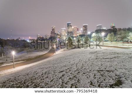 Downtown Houston at  twilight with big and fluffy snowflakes fell on meadow grass at Eleanor Tinsley Park. Park lawn, curved bike pathway, modern skylines in background. Snow is extremely rarely here