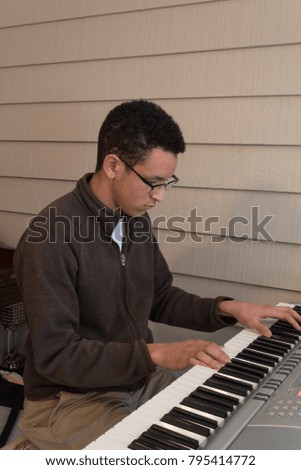 Young mixed race man playing an electric keyboard, seated, neutral background, vertical aspect