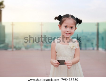 Portrait of child girl in dress with holding something in hands at the rooftop of building.