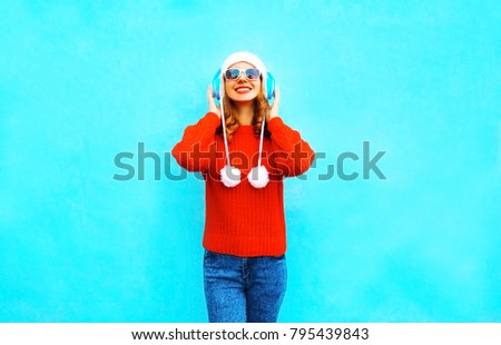 smiling woman in red sweater, listens to music in wireless headphones on blue background