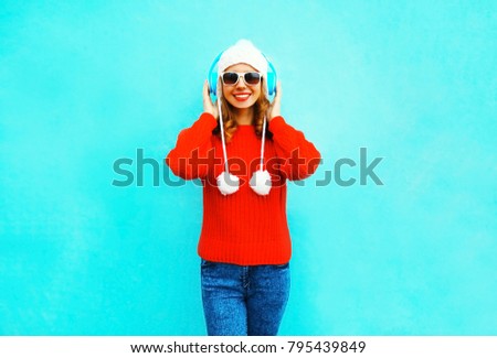 Happy smiling woman in red sweater, listens to music in wireless headphones on blue background