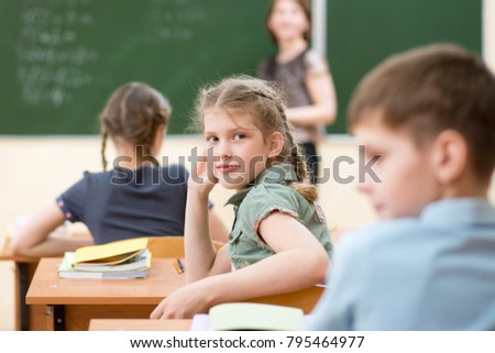 Happy schoolchildren sitting at desk in classroom, teacher at chalkboard
