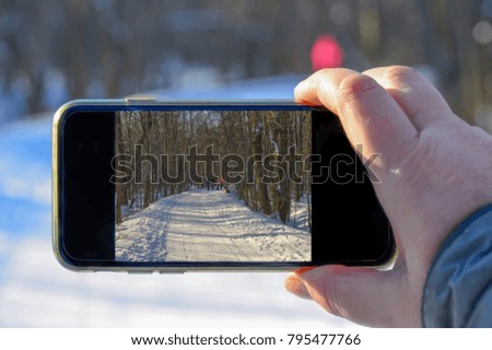 in the winter forest, a picture of the screen of a smartphone photographing the winter nature, and people on the road