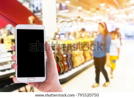 Man use mobile phone, blur image of guitar shop in the mall as background.