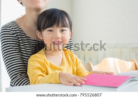 asian little girl reading a book with mom