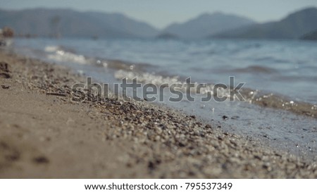 Waves of the sea swim on the sandy beach against the beautiful blurry hills on sunny summer day