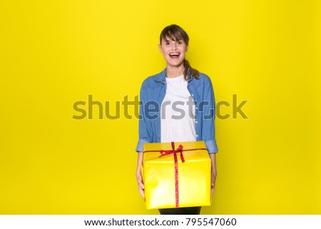 beautiful young woman casual dressed with blue jeans shirt holding a yellow gift box with red ribbon