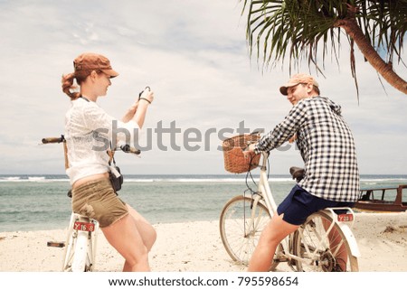 Cheerful woman is having taking pictures her boyfriend in the coast with old fashioned bicycle. Enjoying the company of each other forever.