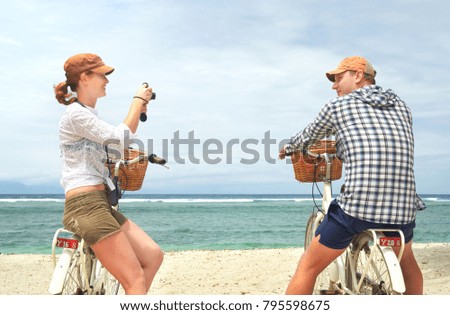 Cheerful couple is having rest and taking pictures in the beach with old fashioned bicycles. Enjoying the company of each other on vacation.
