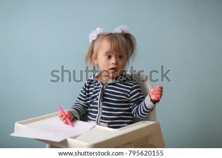 Toddler baby girl with Down syndrome draws in a children's chair, creativity and rehabilitation, lifestyle and toning