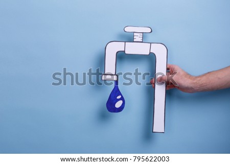 The hand of the man holds a paper image of the tap with a drop of water. Blue background.