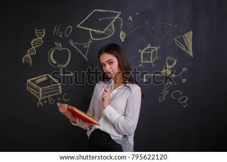 A girl holding a open book, standing by a dark board with signs of science and knowledge.