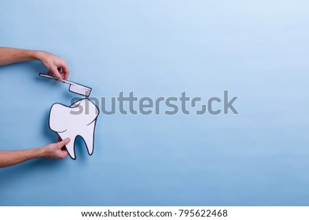The hand of a man holds an image of a tooth and a toothbrush. Blue background with a place for an inscription.