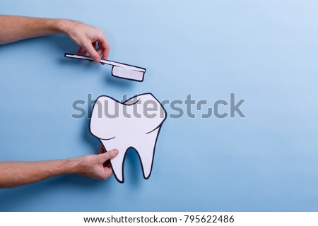 The hand of a man holds a paper image of a tooth and a toothbrush.