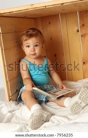 toddler girl reading a book and looking curiously at the camera
