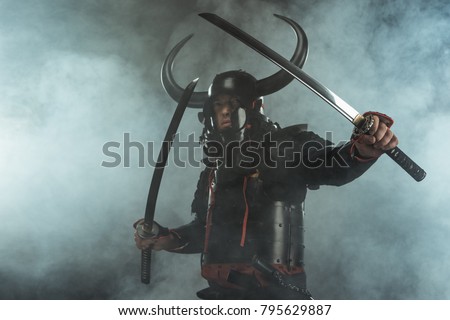 samurai in traditional armor with dual katana swords in defence position on dark background with smoke Royalty-Free Stock Photo #795629887