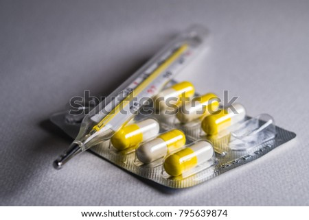 Thermometer and pills on a gray background. Influenza and seasonal illnesses.