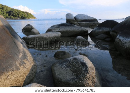 View of the rocky beach in Pulau Perhentian Besar. Big round stones in the calm blue water. Tropical vegetation with palm trees. Calm moment at the end of the afternoon. Picture taken on July 2015. 